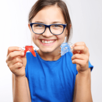 Young girl holding up red and blue retainers