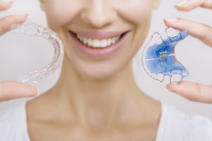 Closeup of smiling woman holding a traditional retainer and modern retainer