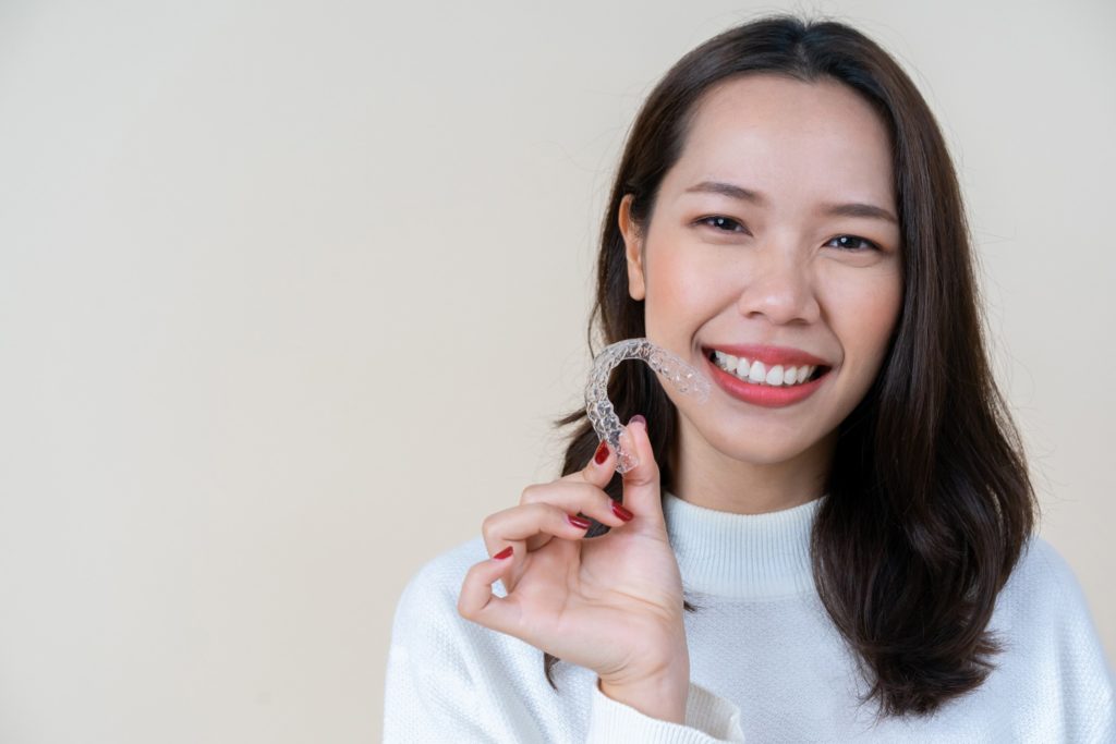 Woman smiling while holding Invisalign retainer