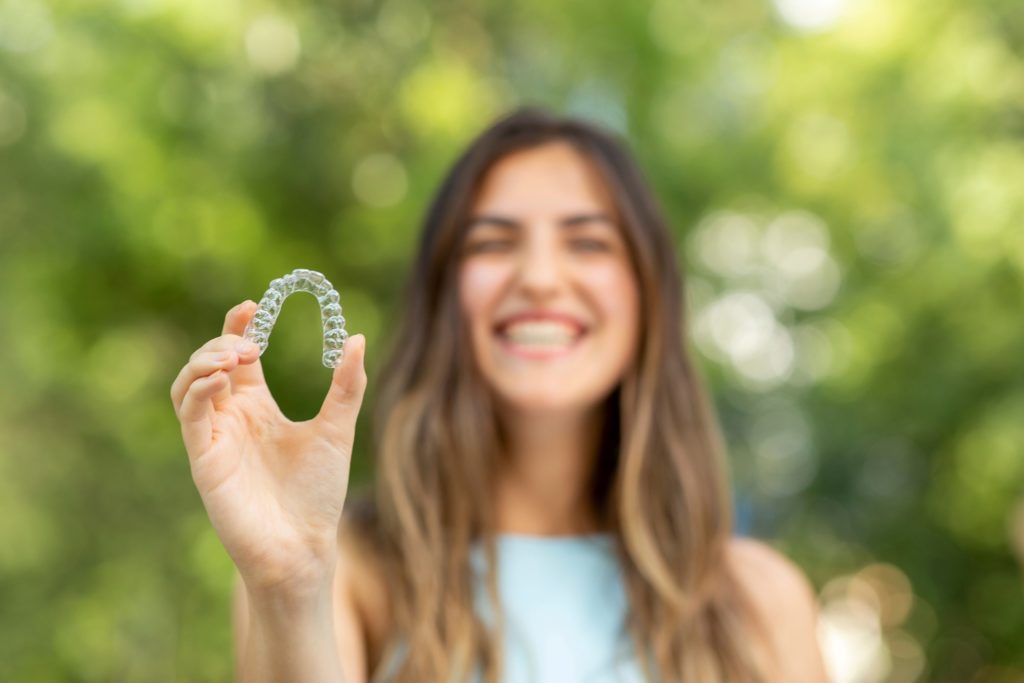 Woman smiling while holding up Invisalign aligner