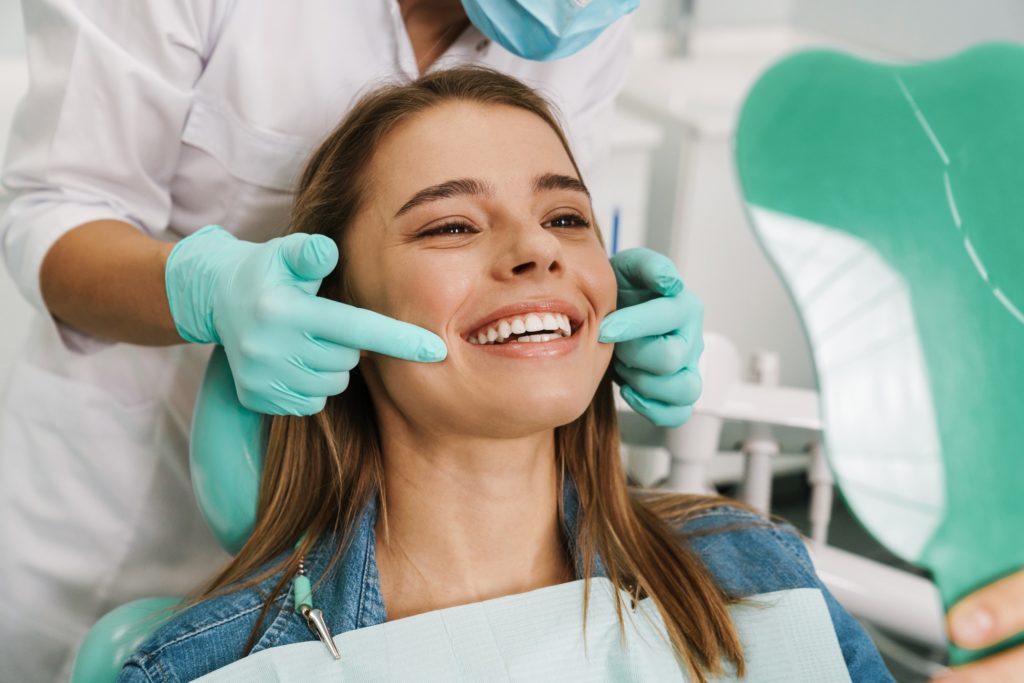 Woman smiling in green mirror after braces removal